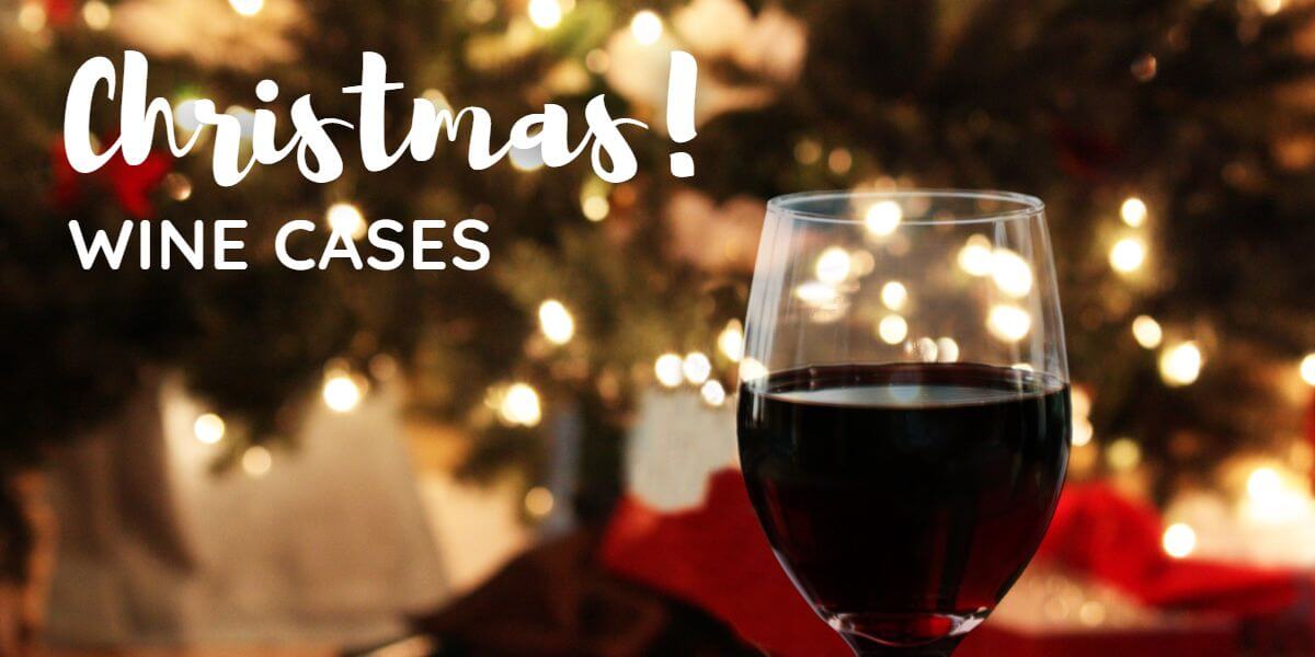 a glass of red wine in the foreground with a nicely decorated Christmas tree all a glow in the background