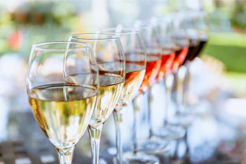 a row of wine glasses ready for a wine tasting. Some filled with white wine, some filled with rose, and some with red wine
