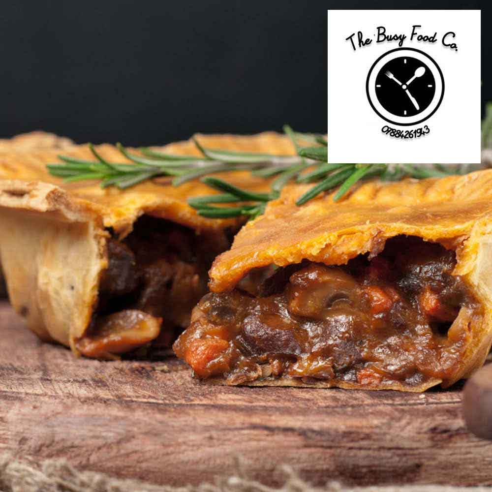 A delicious homemade steak pie on a wooden board, garnished with a sprig of rosemary.
